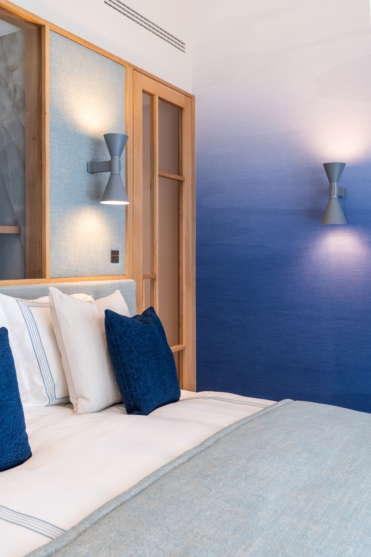 Chambre avec mur bleu profond et tête de lit en chêne, maison de bord de mer en Normandie