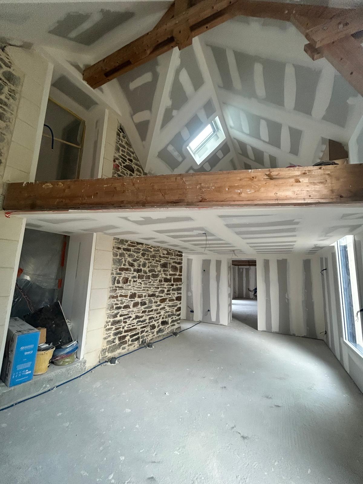 Pièce de vie en cours de rénovation avec poutres et mur en pierre apparent, projet Dol-de-Bretagne